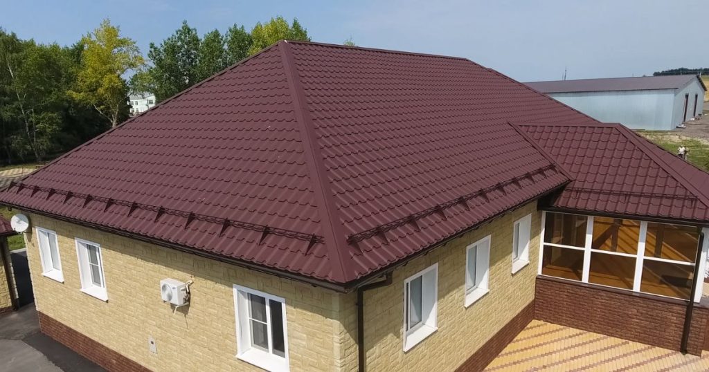 Een roodbruin dak met geïsoleerde dakpanplaten op een woning met een zandkleurige bakstenen gevel met witte ramen en een kleine uitbouw.