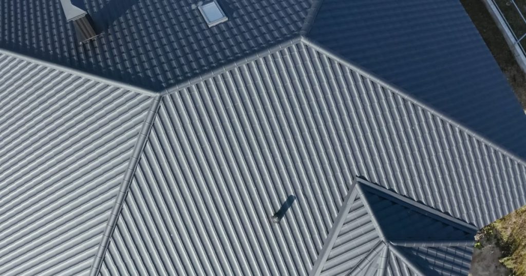 Bovenaanzicht van een dak met sandwichpanelen met trapeziumprofiel. Het dak is grijs. Er zit 1 klein dakraam in het dak.