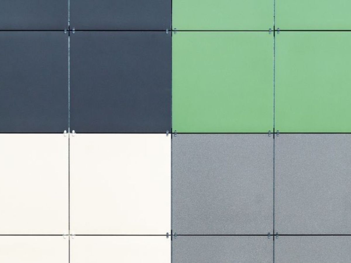 Gevel met keramische panelen in verschillende kleuren, waaronder zwart, wit, groen en grijs, strak bevestigd in een gridpatroon.