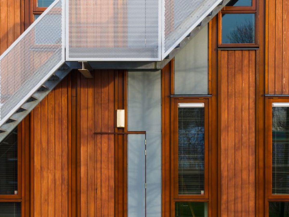 Moderne gevel met verticale houten bekleding, meerdere ramen en een metalen buitentrap.