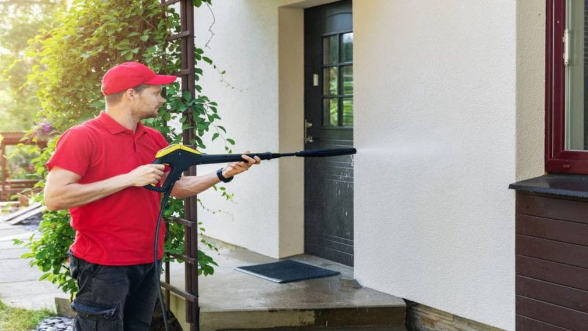 Vakman reinigt een gevel met een hogedrukreiniger bij de voordeur van een woning.