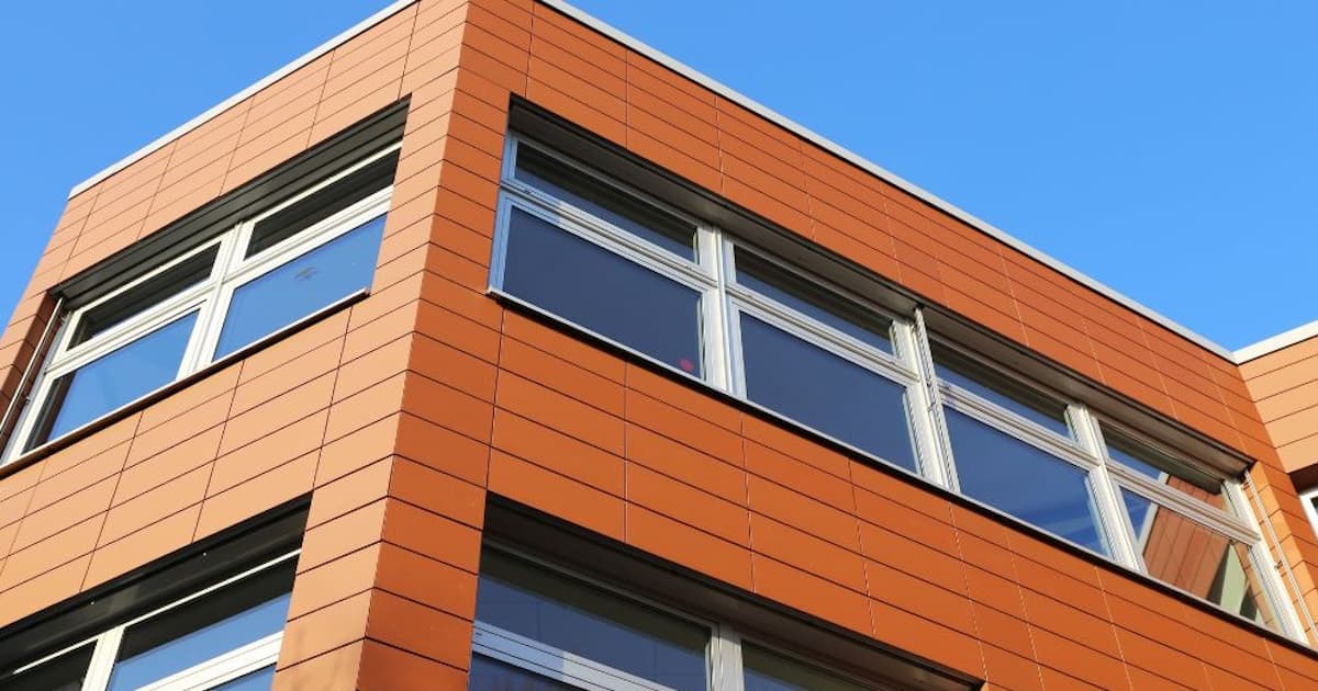 De kunststof gevel van een gebouw met een moderne uitstraling tegen een strakblauwe lucht. De gevelbekleding is gemaakt van kunststof. 