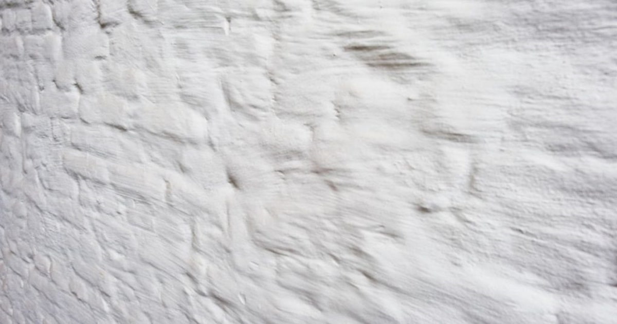 Een bakstenen muur met een witte laag kalei. De structuur van de bakstenen is nog goed zichtbaar.