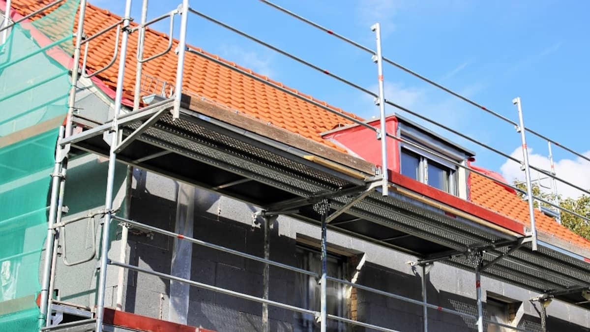 De renovatie van een gevel. Om de woning zijn steigers geplaatst zodat de gevelwerkers op hoogte kunnen werken. Tegen de gevel van het huis is isolatie zichtbaar. Op het dak liggen oranje dakpannen.
