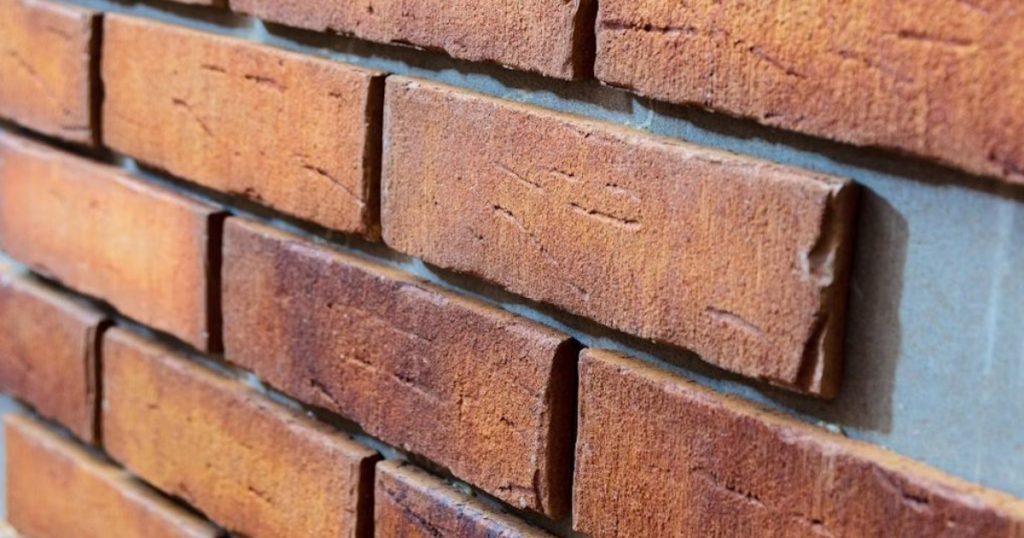 Een close-up van rode steenstrips tegen een gevel. Doordat rechts een van de strips nog ontbreekt kun je de geringe dikte goed zien.