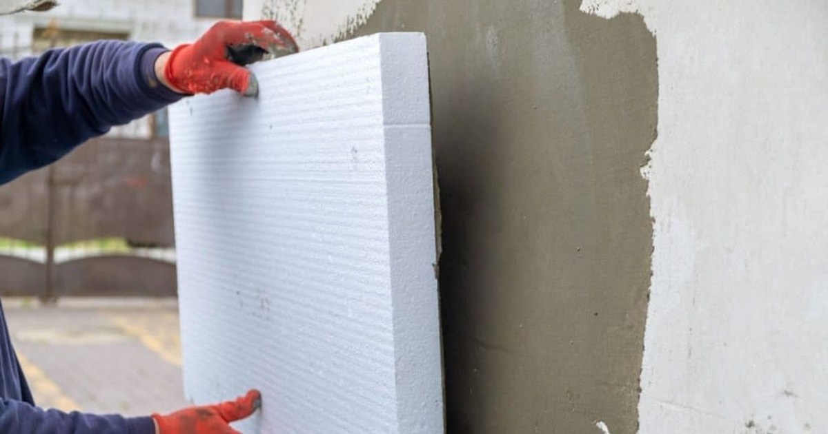 Een gevelspecialist plaatst een isolatieplaat tegen een onafgewerkte gevel. De expert draagt rode handschoenen.