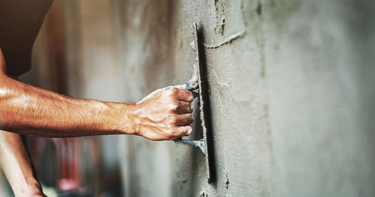 Een close-up van het aanbrengen van sierpleister met een spaan. De sierpleister is grijs van kleur.