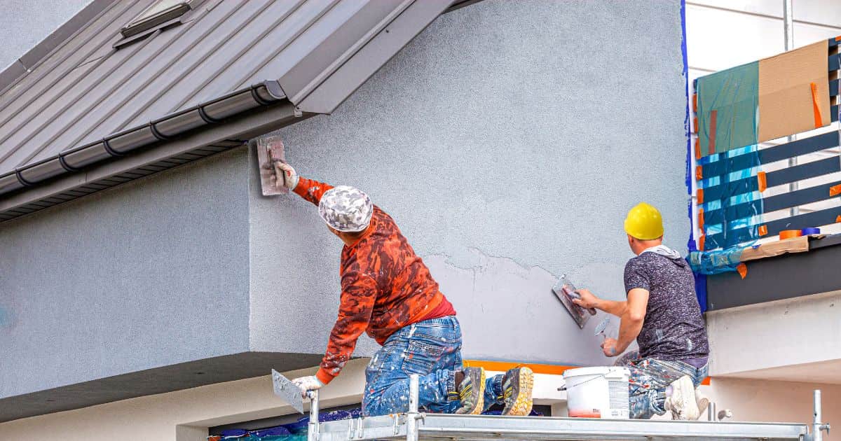 Twee gevelwerkers werken op een steiger om een sierpleister tegen een gevel aan te brengen. 