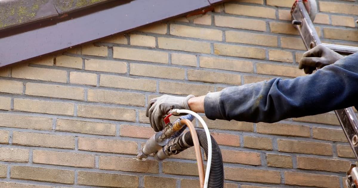 Een gevelspecialist isoleert de spouwmuur door spouwmuurisolatie in te blazen. Daarvoor is een kleine opening in de gevel gemaakt.