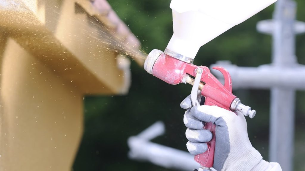 Gevelkurk wordt met een rood spuitpistool tegen de gevel gespoten. De gevelwerker draagt een lichte handschoen.