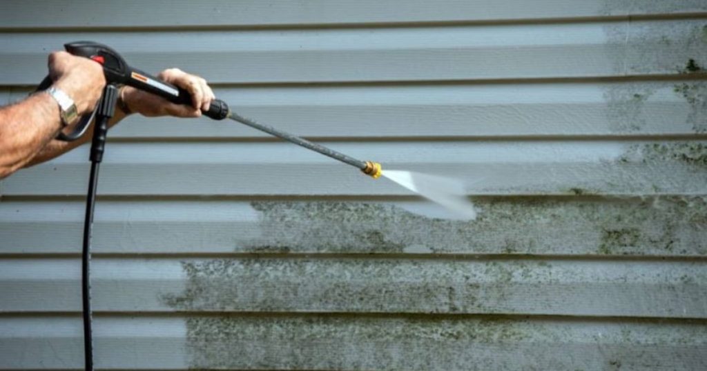 Een man reinigt groene aanslag op de gevelbekleding met een hogedrukreiniger. 