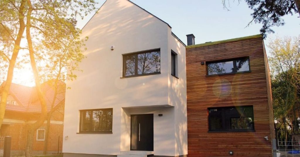 Een woning met twee soorten gevelbekleding. Links zien we een witte sierpleister, rechts moderne houten gevelbekleding met een warme tint.