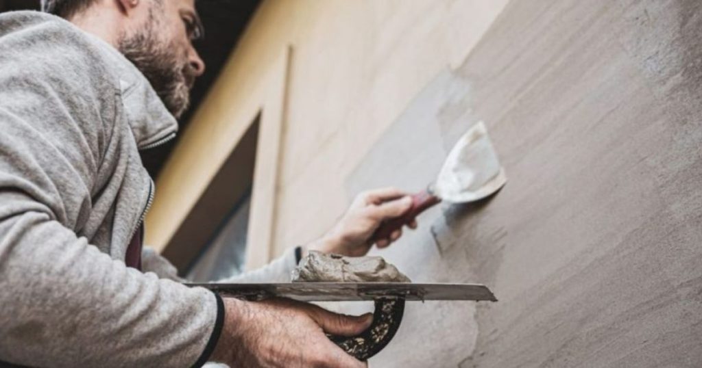 Gevelspecialist brengt pleister aan op een buitenmuur tijdens gevelrenovatie.