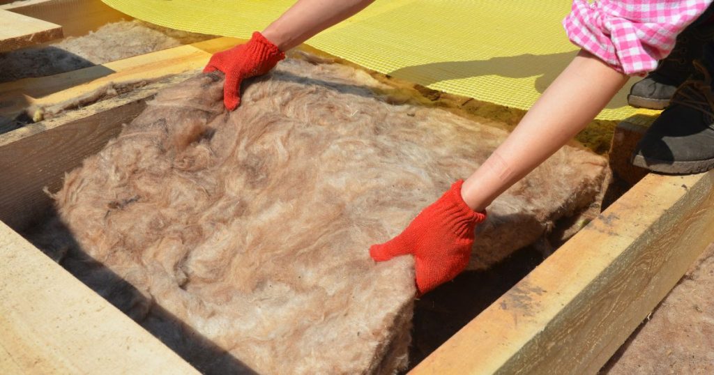 Een dakspecialist plaatst schapenwol dakisolatie (een ecologisch alternatief op glaswol) op de zoldervloer van een hellend of schuin dak.