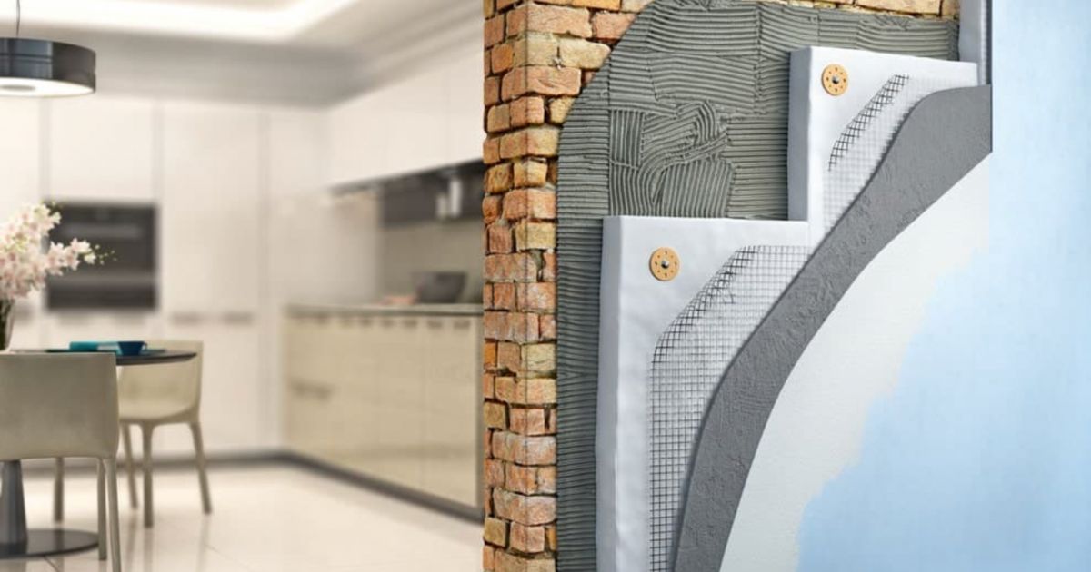 Een doorsnede van een buitenmuur is te zien met de verschillende lagen isolatie en gevelpleister. Aan de linkerkant van de muur is een keuken te zien.