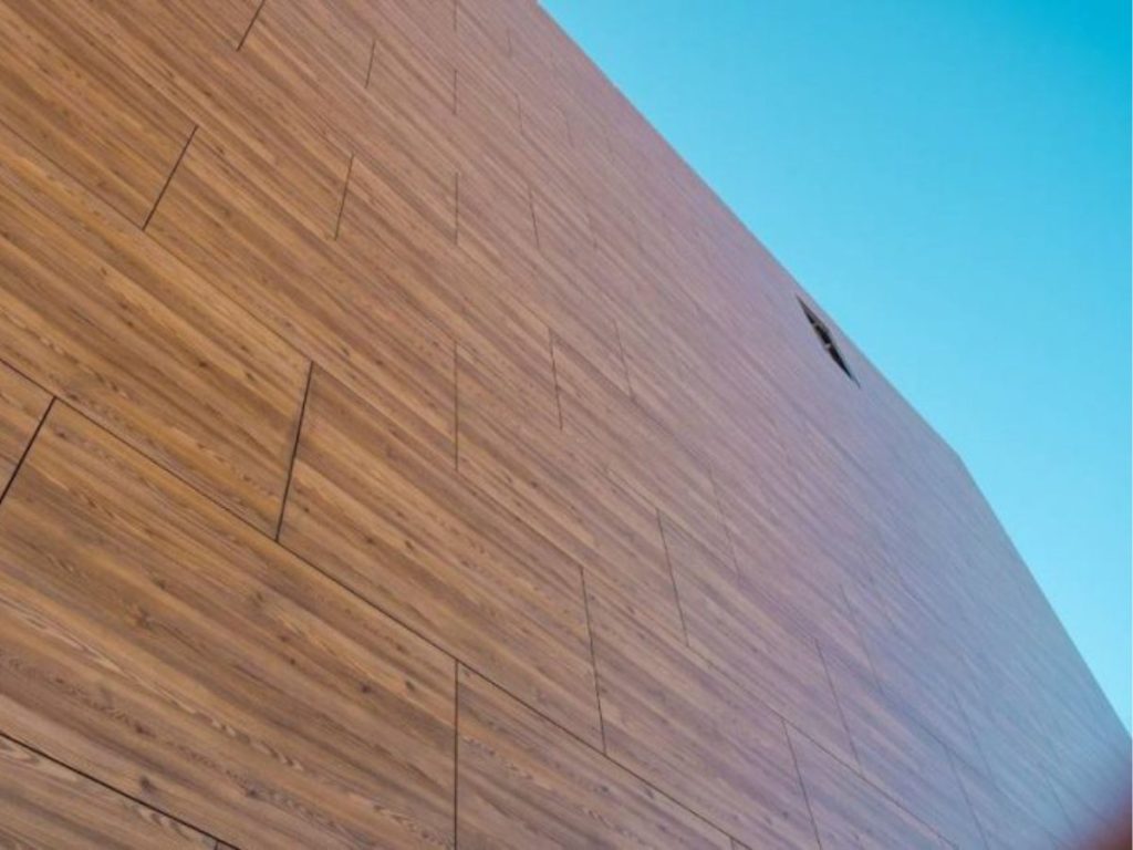 Moderne gevel met HPL-gevelbekleding in houtlook, strak geplaatst tegen een helderblauwe lucht.