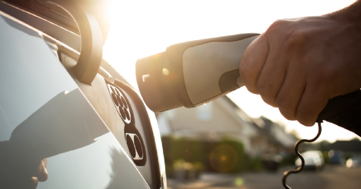 Een hand laadt de accu van een elektrische wagen op met zonne-energie.