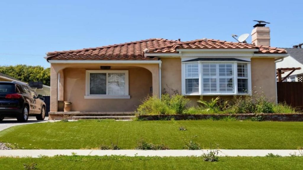 Een woning in een landelijke stijl met een gevel van een warme tint kalei. Er is een gazon op de voorgrond zichtbaar en een donkere auto staat aan de linkerkant van het huis geparkeerd. 