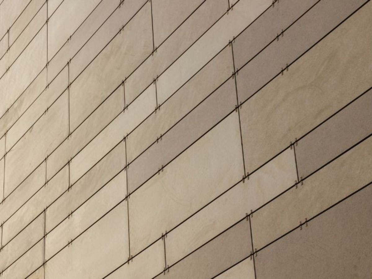 Close-up van keramische gevelbekleding met rechthoekige platen en zichtbare bevestigingselementen.