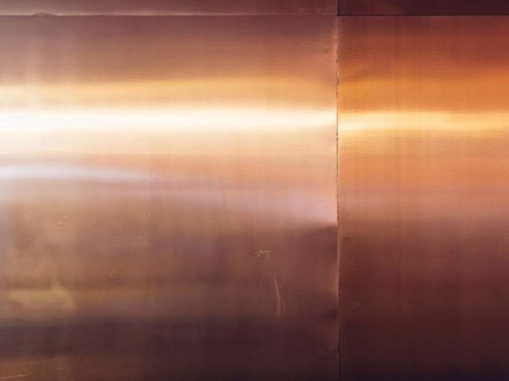 Close-up van koper gevelbekleding met een warme glans en zichtbare lasnaden.