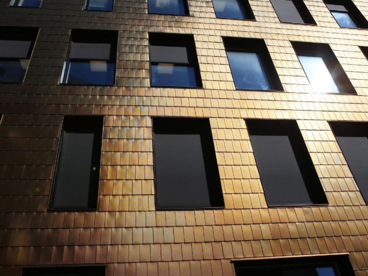 Gevel van een gebouw met koperkleurige gevelbekleding, waarbij de zon het oppervlak verlicht en de ramen zichtbaar zijn.