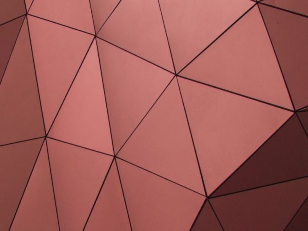 Close-up van koperen gevelpanelen in een modern driehoekig patroon met strakke lijnen.