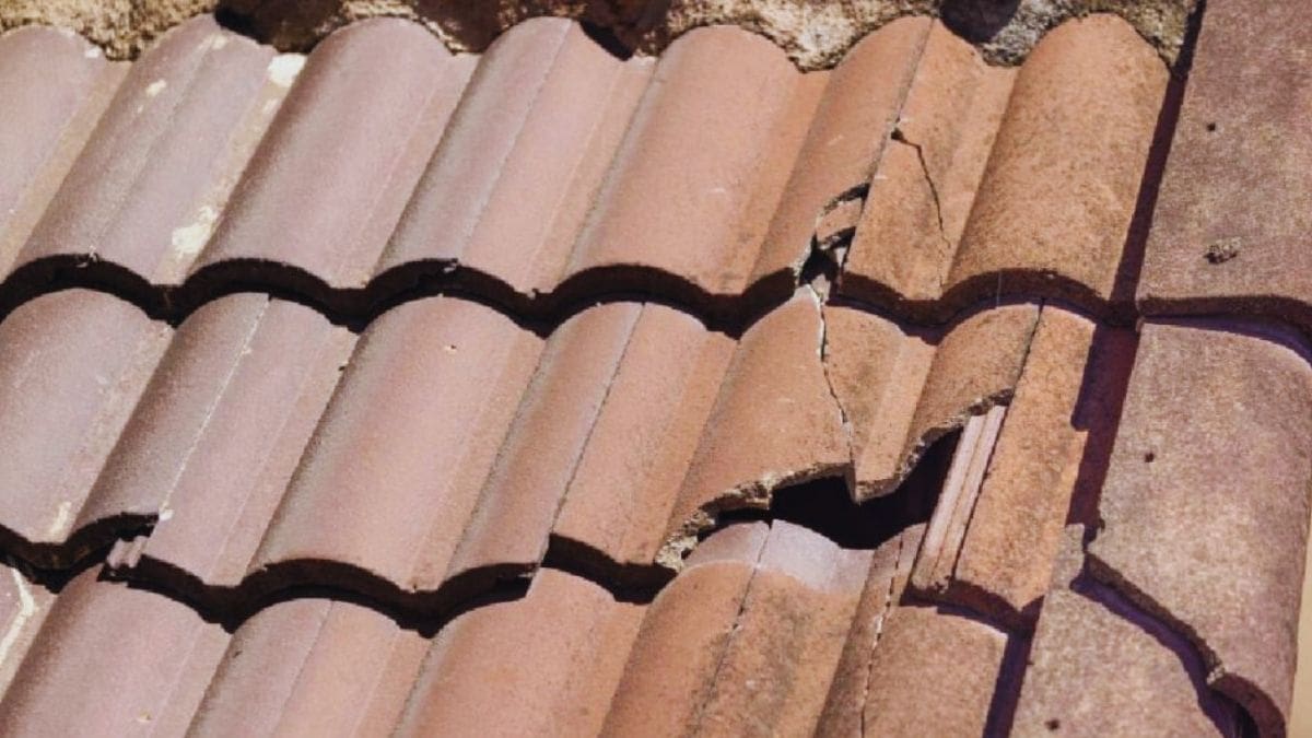 Een dak met beschadigde oranje betonnen dakpannen die vervangen moeten worden om de minimale levensduur van het dak te garanderen.