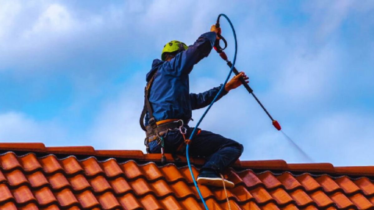 Een dakwerker sproeit een nieuwe coating op betonnen dakpannen om hun levensduur te verlengen en de pannen te beschermen tegen vocht.