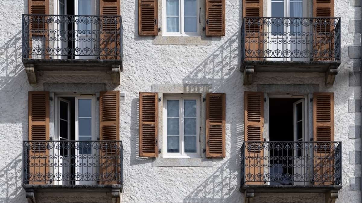 Een grijze sierpleister gevel gecombineerd met houten luiken en gietijzeren hekwerk. 