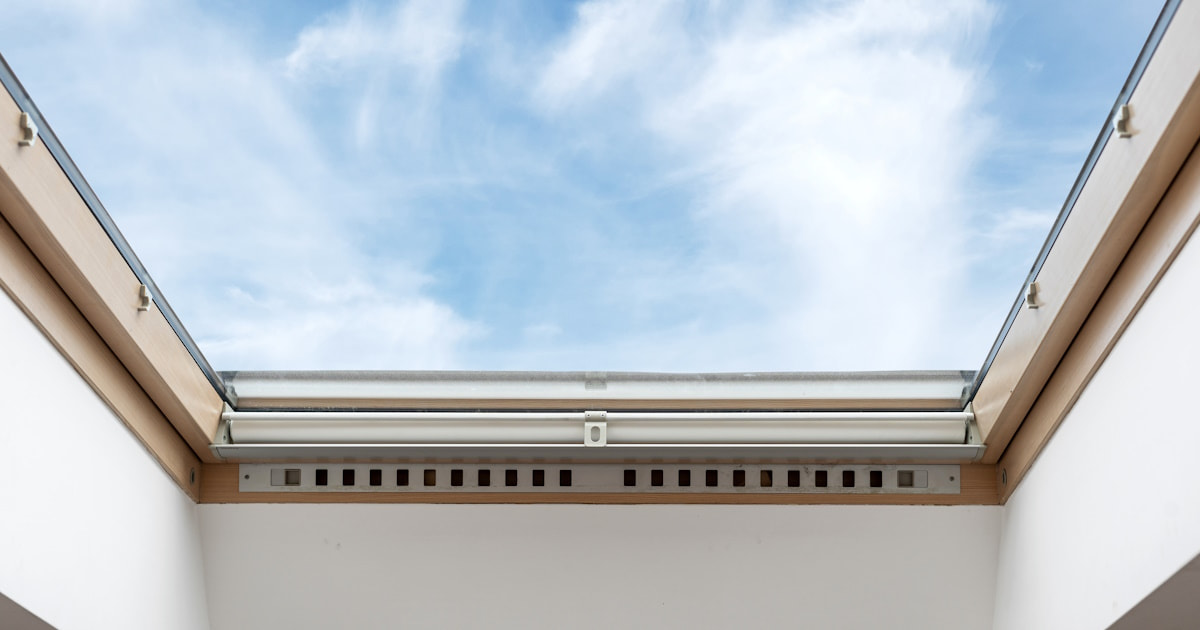 Een brede lichtstraat in een houten frame. Op de achtergrond een bewolkte lucht.
