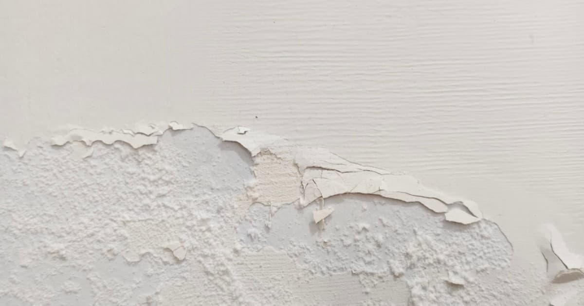 De witte wandafwerking laat plaatselijk los en onthult de beschadigde ondergrond van de muur.