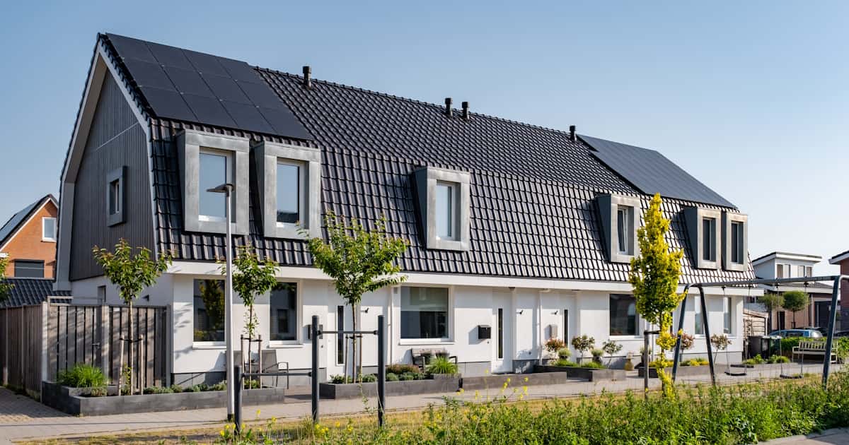 Een aantal rijwoningen met een gedeeld mansardedak. De dakbedekking bestaat uit dakpannen, op het dak liggen zonnepanelen