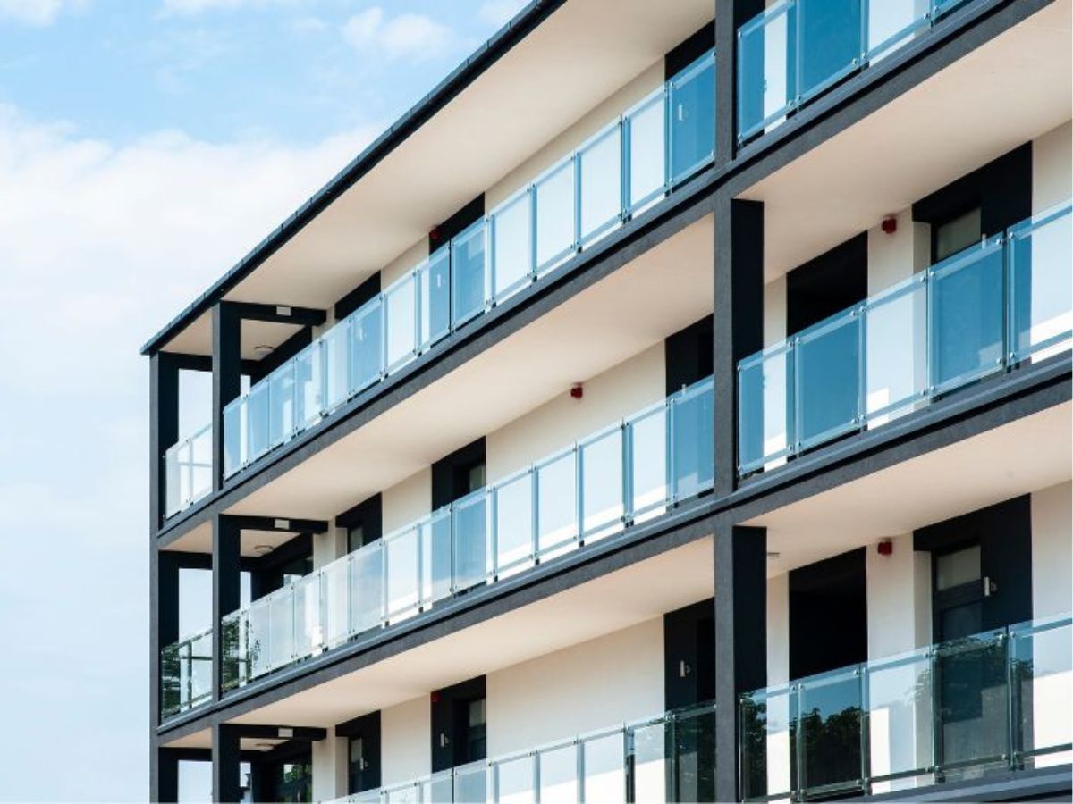 Modern appartementencomplex met kunststof gevelbekleding met uitstraling van steen en glazen balkonhekken, strak ontwerp tegen een blauwe lucht.