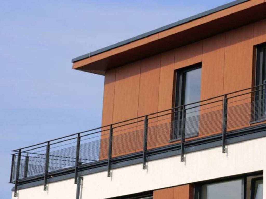 Moderne woning met HPL-gevelbekleding en metalen balkonleuning tegen een blauwe lucht.
