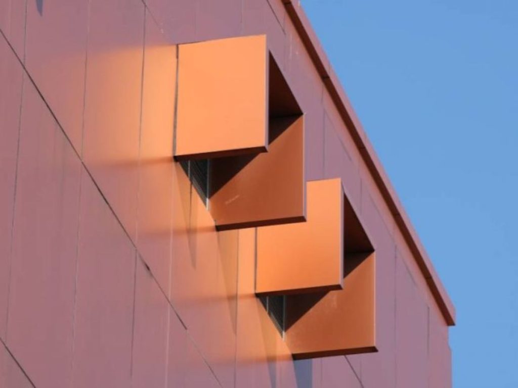 Moderne gevel met koperbekleding en uitstekende vierkante raamelementen tegen een blauwe lucht.
