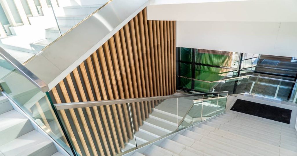 Moderne trap met verticale houten latten als lambrisering en een glazen balustrade met metalen trapleuning.