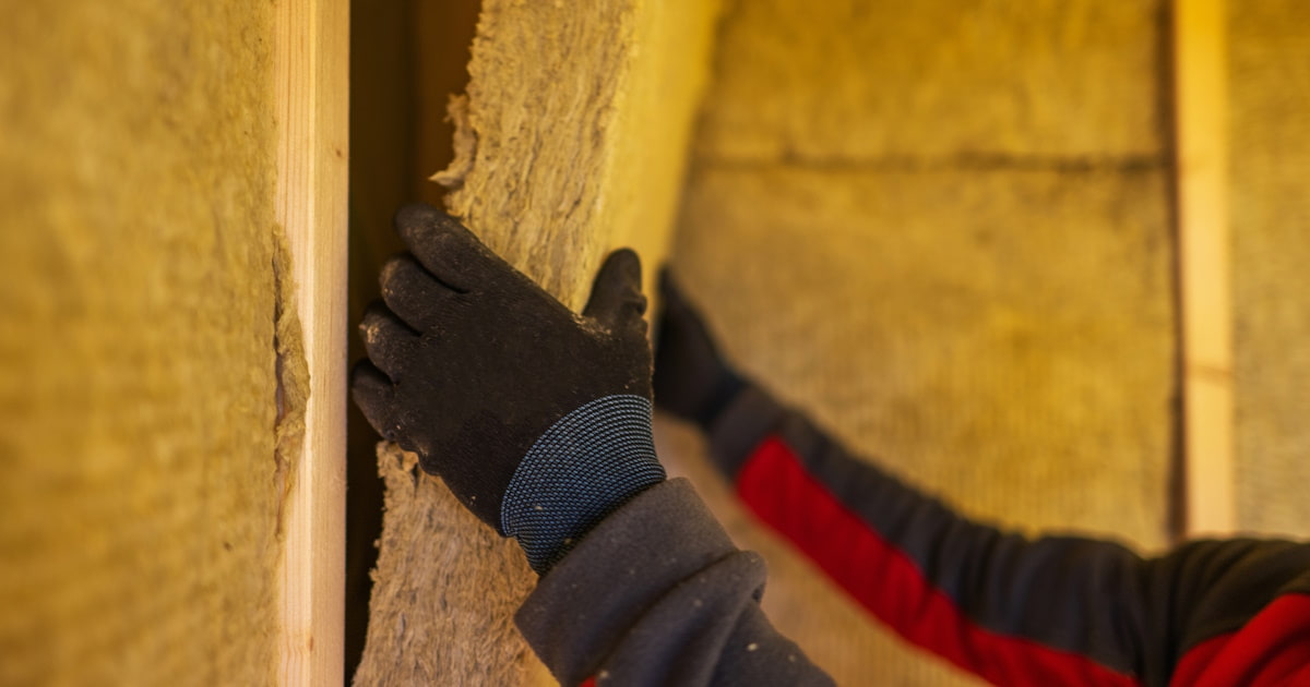 Een isolatiespecialist draagt beschermende kleding om isolatiemateriaal aan te brengen