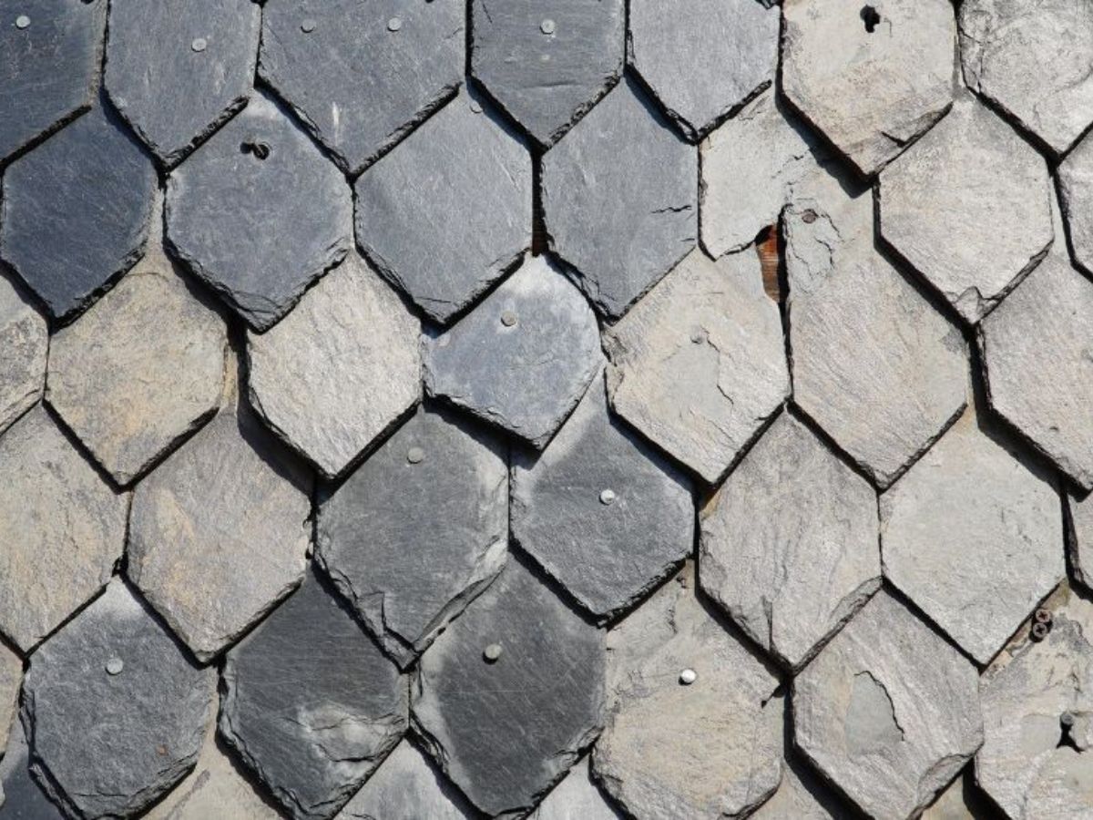 Close-up van gevelbekleding met natuurleien in overlappend patroon, bevestigd met zichtbare nagels.