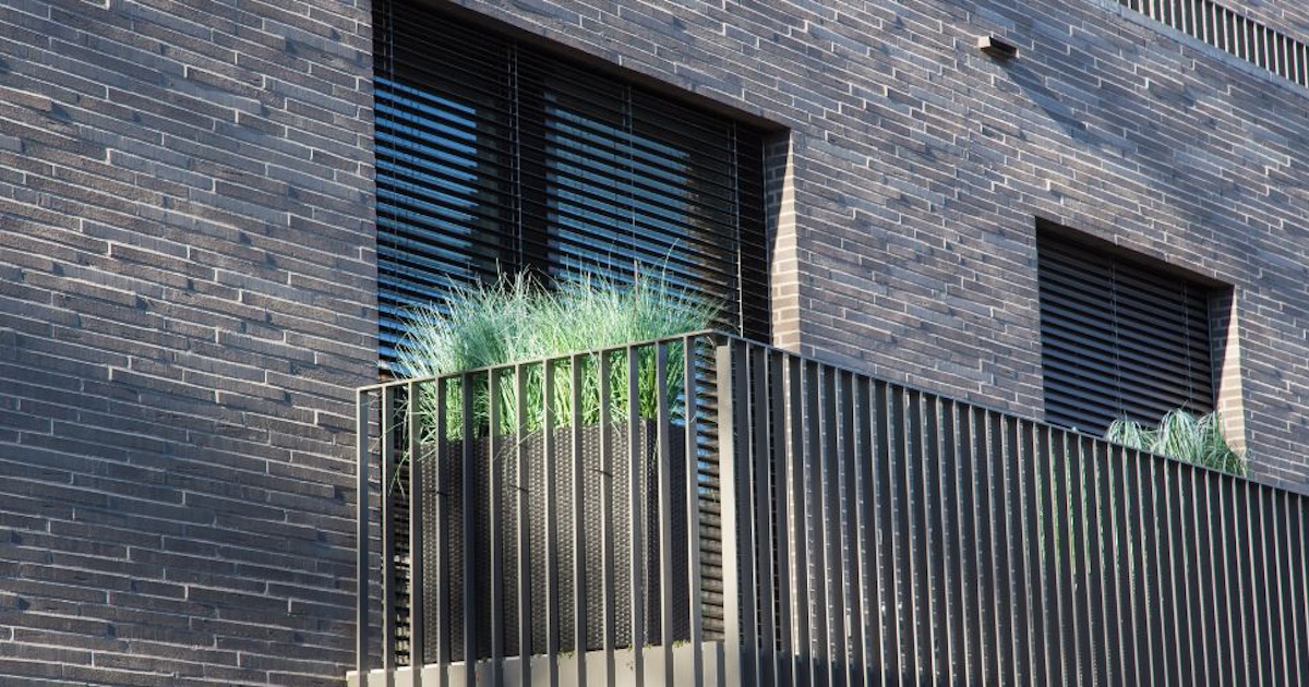 Een moderne grijze gevel gemaakt van smalle natuurstenen. De gevel is gecombineerd met metalen elementen.