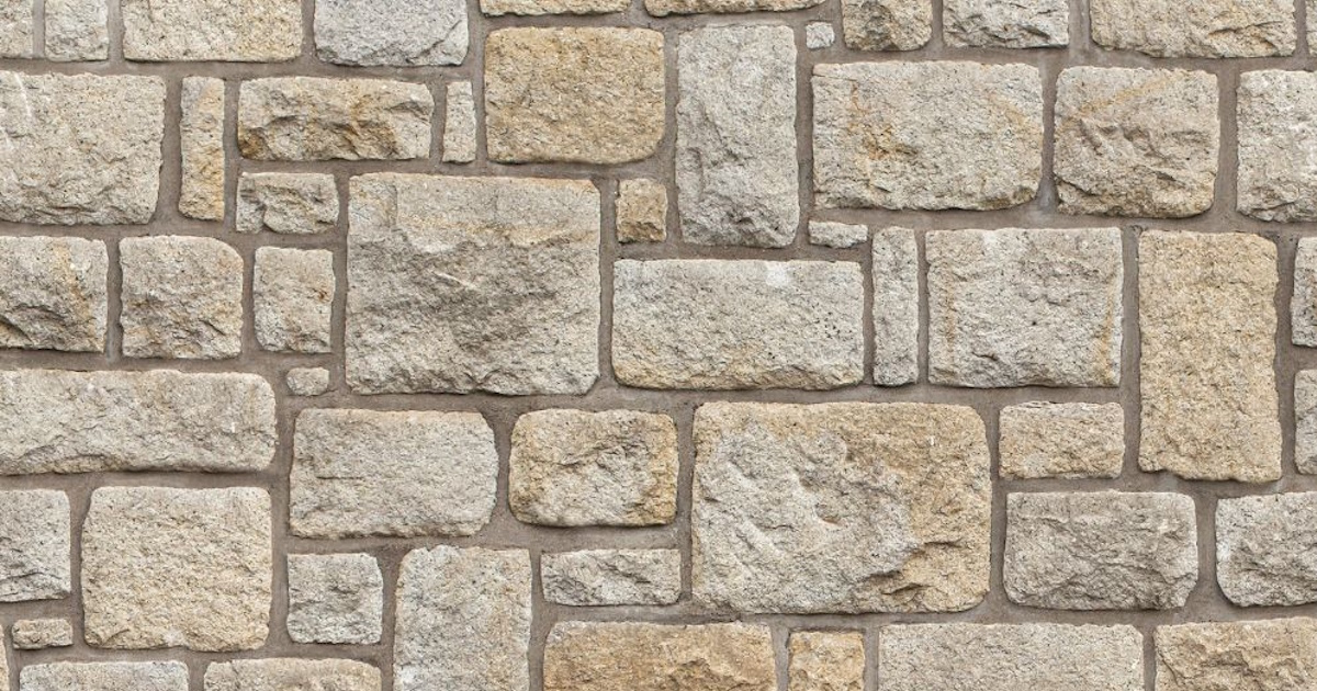 Een close-up van een natuursteen gevel met een beige kleur. De stenen hebben verschillende groottes en vormen.