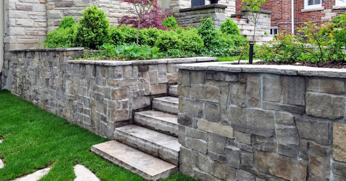 Een trap en wat muren gemaakt van grijze natuursteen. Het contrast met de groene planten en het gazon is sterk.