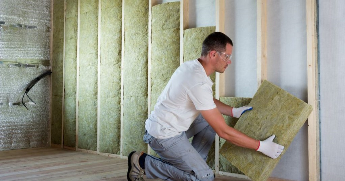 Een isolatiespecialist plaatst minerale wol tegen een binnenmuur. De expert draagt een veiligheidsbril en handschoenen.