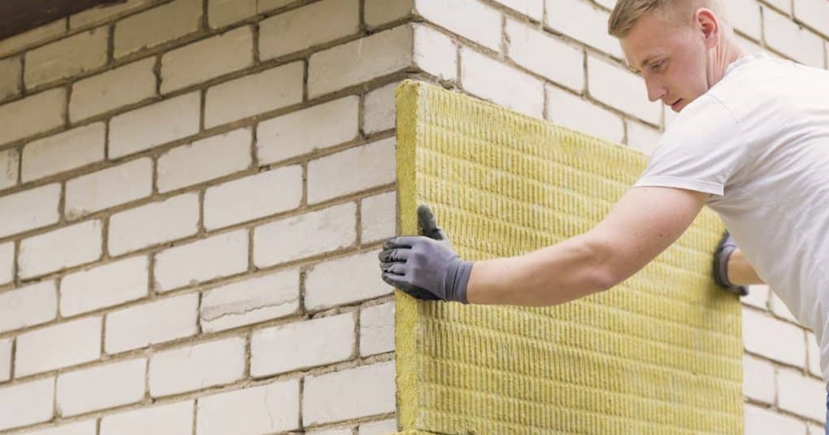 Een gevelspecialist is bezig met het plaatsen van gevelisolatie. Hij draagt er beschermende handschoenen voor.