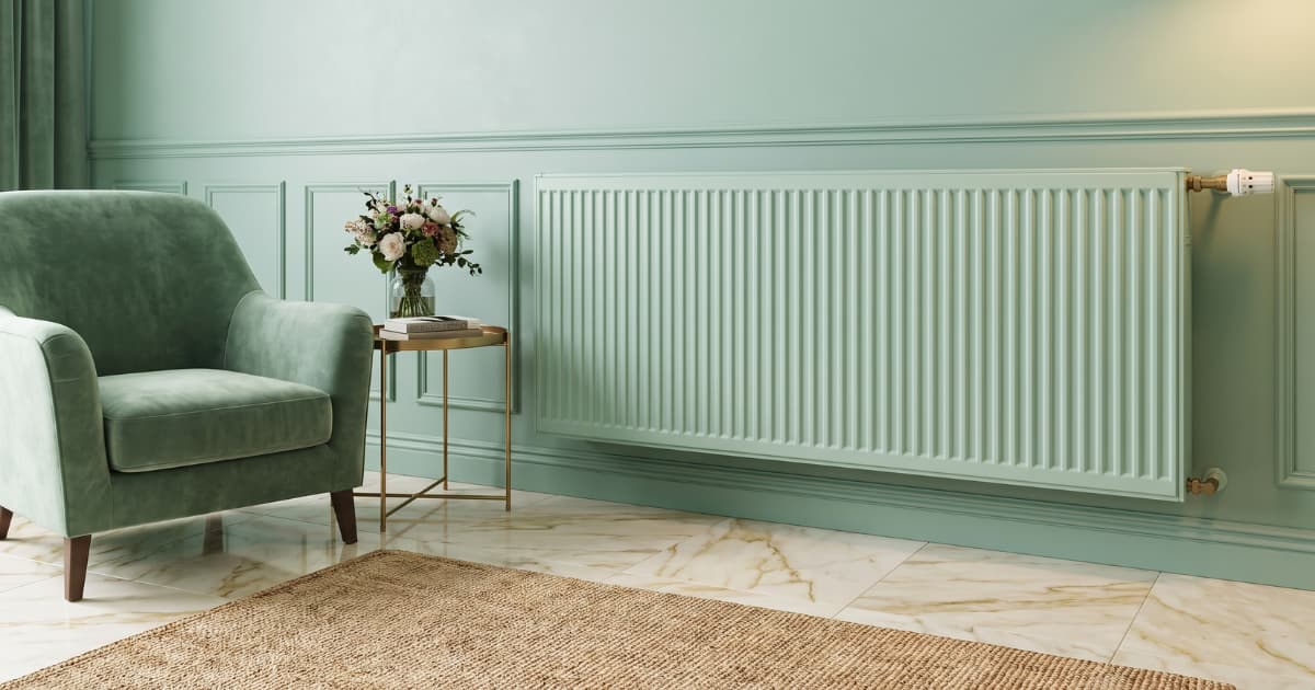 Een paneelradiator in dezelfde mintgroene kleur als de muur met lijstwerk valt rustig weg naast een groene fauteuil en een gouden bijzettafel met bloemen.