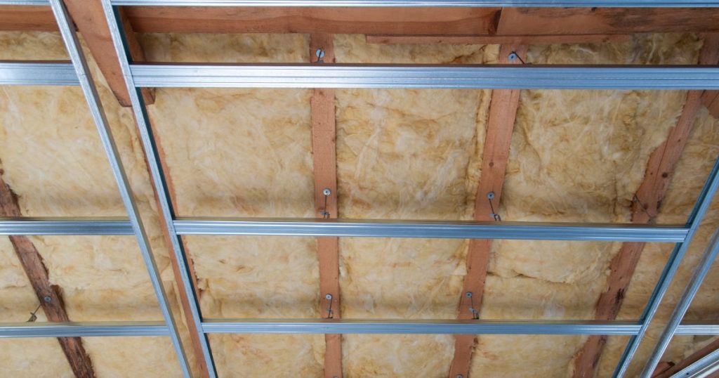 De binnenzijde van een plat dak, met een dikke laag minerale wol als isolatie tussen de houten balken van de dakconstructie. Een metalen raamwerk dient als bevestiging voor het dampscherm en de binnenafwerking van het plafond.