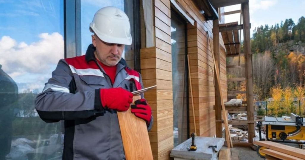 Een vakman renoveert een gevel en gebruikt daar houten gevelbekleding voor. Hij draagt handschoenen en een veiligheidshelm.