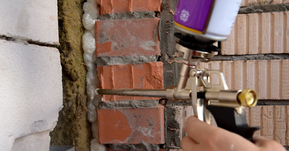 Met een spuitpistool wordt een kier tussen isolatie en een bakstenen muur gedicht