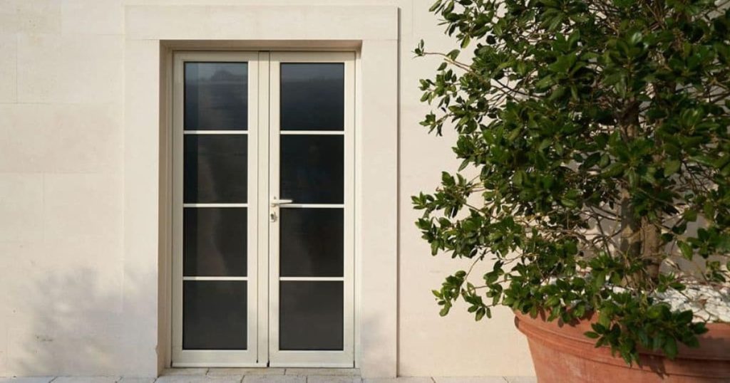 PVC-deur met glaspartijen in witte gevel naast grote plantenbak.