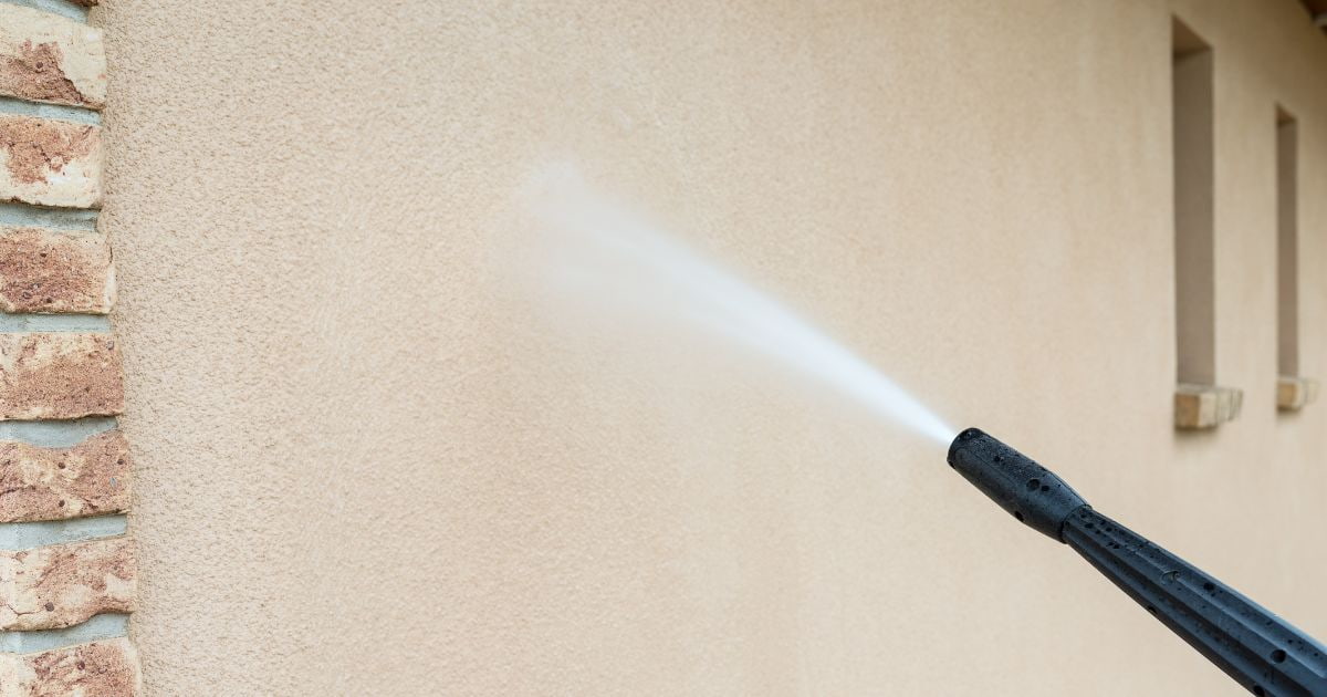 Met een hogedrukreiniger wordt de sierpleister gevel van een woning gereinigd.
