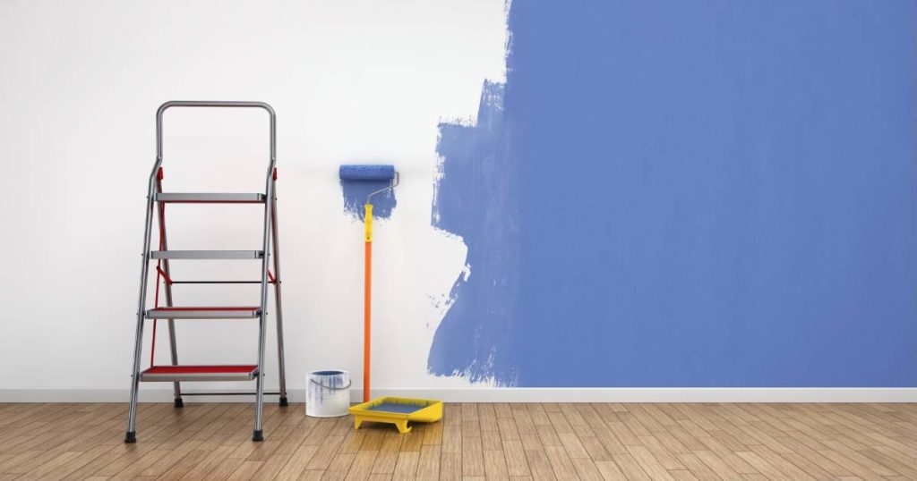Een half geschilderde muur met blauwe verf, een verfroller en een ladder. 